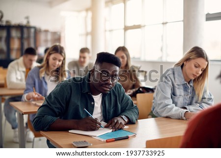 Black university student taking notes during lecture in the classroom. 