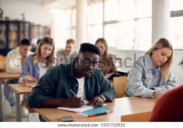 Black university student taking notes during lecture in\
the classroom. 