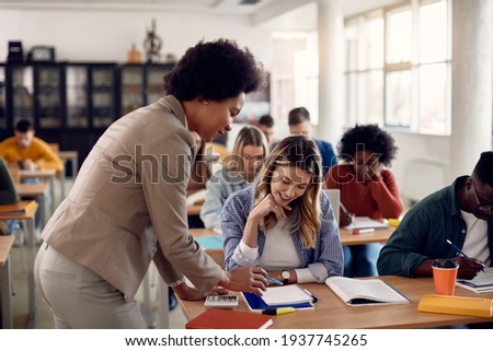 Black university teacher assisting her female student with a lecture in the classroom. Focus is on student. 