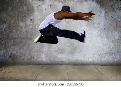 Black Urban Hip Hop Dancer Jumping High On A Concrete Background.  The Man Is Doing Parkour Or Leaping.