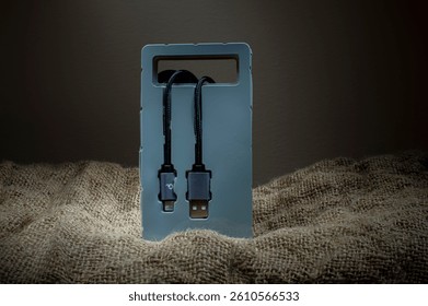 Black USB cable in plastic packaging on fabric background. Copy space.