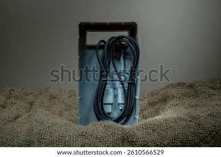 Black USB cable in plastic packaging on fabric background. Copy space.
