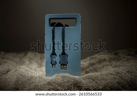 Black USB cable in plastic packaging on fabric background. Copy space.