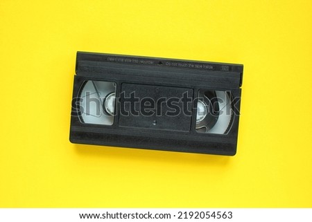 Black VHS videotape recorder cassette on yellow background. Old obsolete technology for tape recording and watching media movies. Retro, vintage, history, nostalgia concept. Top view, flat lay