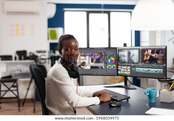 Black videographer smiling at camera editing\
video project in post production software working in creative\
studio office. African movie maker editing audio film montage on\
professional computer