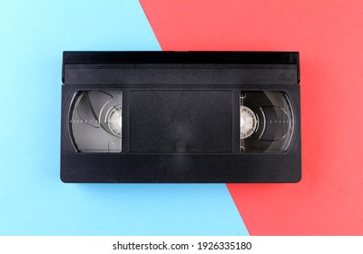Black Videotape On A Red And Blue Background. Retro Technology Of Recording Video On Tape
