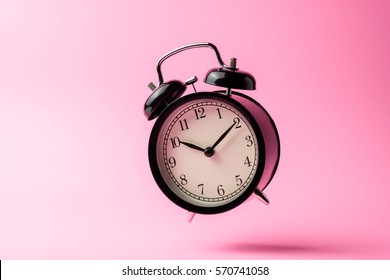 black vintage alarm clock floating on the air with pink color background