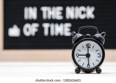 black vintage alarm clock on the background of signs with the inscription in English in the nick of time