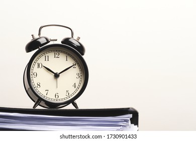 Black vintage alarm clock on paper files stacked in black folder isolated on white wall background. - Powered by Shutterstock