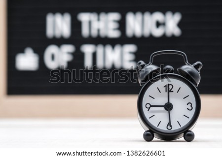 black vintage alarm clock on the background of signs with the inscription in English in the nick of time