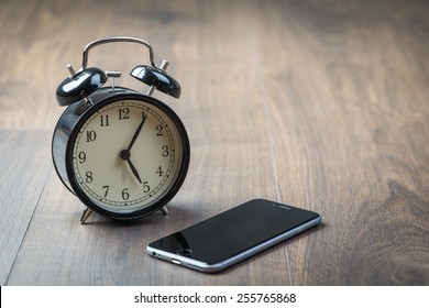 Black Vintage Alarm Clock With Phone On A Wooden Floor