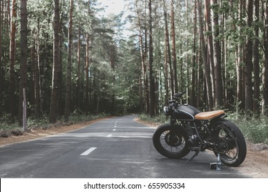 Black vintage custom motorcycle motorbike caferacer standing in the forest road during sunset - Powered by Shutterstock