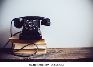 Black Vintage Rotary Phone And Books On Rustic Wooden Table, On A White Wall Background