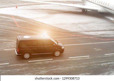 Black VIP service van running on airport taxiway with blurred private jet on background. Business class service at airport. Security intelligence agency hurrying at airfield