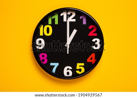 black wall clock with 
Colorful Numerals on yellow background show one o'clock