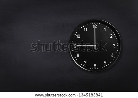 Black wall clock showing nine o'clock on black chalkboard background. Office clock showing 9am or 9pm on black texture