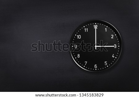 Black wall clock showing three o'clock on black chalkboard background. Office clock showing 3am or 3pm on black texture