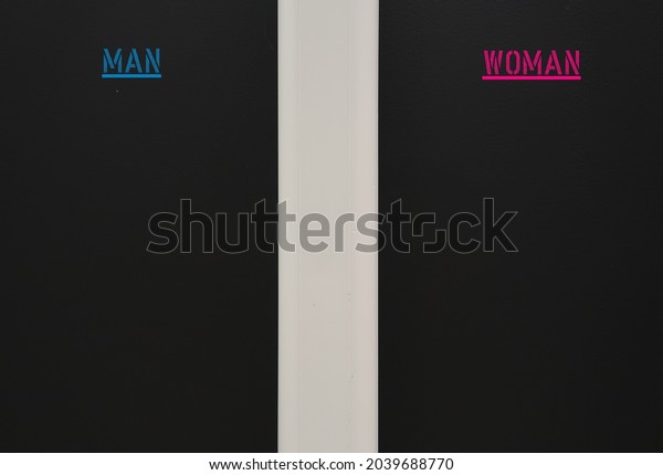 A black wall divided by a pipe with blue and\
pink text MAN and WOMAN  , concept of opposite sex and gender, \
difference between male and female leads to different attitude\
expectations or perceptions