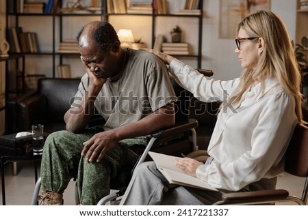 Black war veteran in wheelchair experiencing stress at therapy session, psychologist consoling him