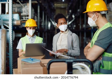 Black Warehouse Manager Talking To Her Employees While Examining Shipment Schedule At Storage Room During Coronavirus Pandemic.