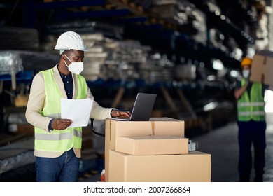 Black Warehouse Manager Working On Laptop And Wearing Face Mask Due To Coronavirus Pandemic.