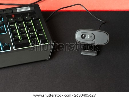 A black webcam on a computer desk. Webcam and keyboard.