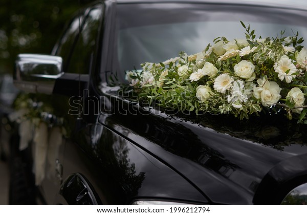 A black wedding car decorated with white roses,\
bridal bouquet, just married