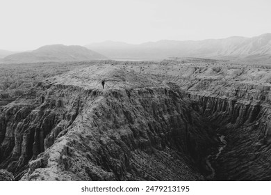 Black and white adventurous solo traveler hikes a scenic canyon path. Dark valley unfolds below, with peaks in the distance of the inspiring travel scene.  - Powered by Shutterstock