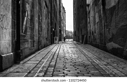 A black and white analogue image of a lonely figure walking down an old alleyway in Glasgow town center - Powered by Shutterstock