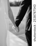 Black and white artistic digital photo of bridegroom in dark suit and white shirt in wedding marriage holding hands with the bride in white long wedding bridal dress.