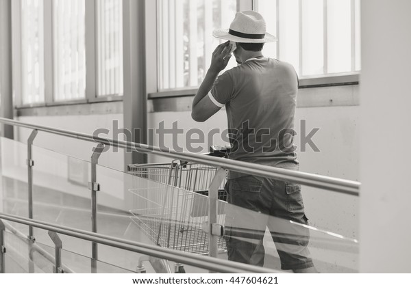 Black\
and white back view of male person walking talking on mobile smart\
phone during shopping. Cart on store\
background.