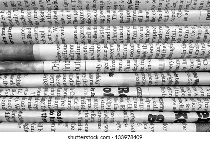 A black and white background of English language newspapers stacked and folded in a horizontal position and viewed in close up