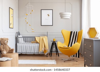 Black and white blanket on yellow egg chair in grey baby bedroom with black wooden stool with mug and grey crib with cozy blanket