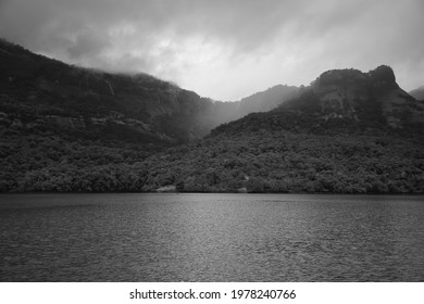 Black and white breadth taking mountain ranges covered with forest surrounded by lake during monsoon season sky covered with clouds in vacation holiday trek at India