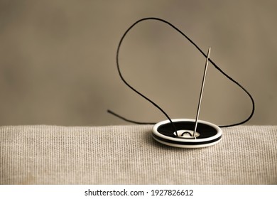 The black and white button is sewn with a sewing needle and black thread to hold the two fabrics together in close-up. A vintage-style photo for an article about the sewing hobby and sewing.