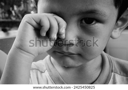 Black and white close up image of cute little toddler boy. Portrait of sad kid covering his eyes with hands. Child looking at camera. Horizontal monochrome photo.