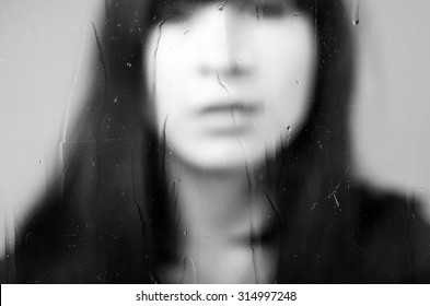 Black and white closeup diffused portrait of brunette girl behind glass concept of melancholy, sadness, loneliness