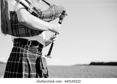 Black and white closeup of male in Scottish traditional kilt playing bagpipe on summer outdoors background