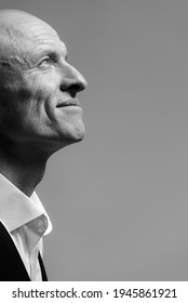 Black And White Close-up Portrait Of A Smiling Bald Middle-aged Man In Profile. Business Man On A Gray Background.