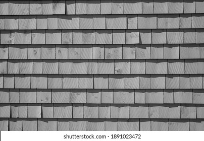A black and white closeup of rows of weathered wooden shingles on the side of an old wooden house.