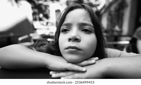 Black and white close-up of a young girl resting her chin on her hands, gazing thoughtfully into the distance. moment of introspection in a natural outdoor setting - Powered by Shutterstock