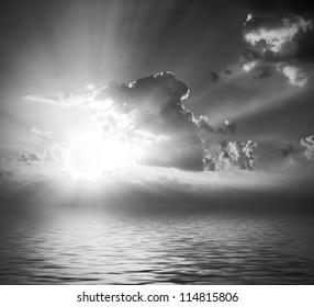 black and white cloudy sunrise (sunset) with sunbeams, clouds and reflection in water surface - Powered by Shutterstock