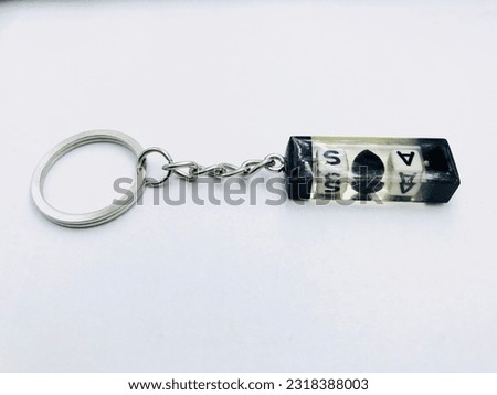 A black and white colour, rectangle shape keytag on white background.It has A and S letter, small heart, silver keychain. It made of resin material. This picture was taken from the side of the keytag.