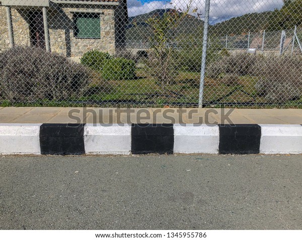 Black\
and white concrete curb with asphalt road \
close-up