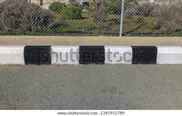 Black\
and white concrete curb with asphalt road \
close-up