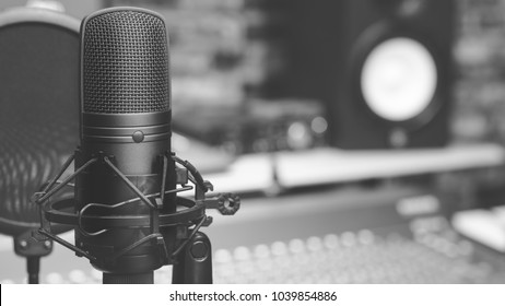 black and white condenser microphone on audio mixing board & studio monitor speakers background. recording concept