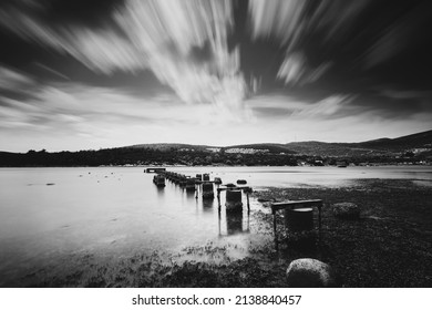 Black And White Daytime Long Exposure With Neutral Density Filter Of An Old And Shattered Concrete Pier And Cloudy Horizon.