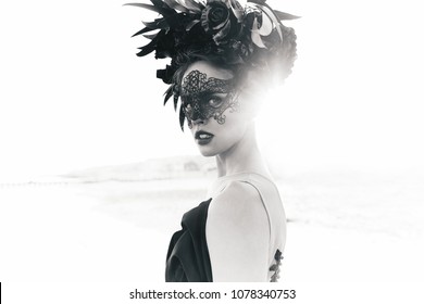 Black and white dramatic portrait of beautiful young woman in dress with black flowers and with black lace mask on face and floral crown on head. Sea background - Powered by Shutterstock