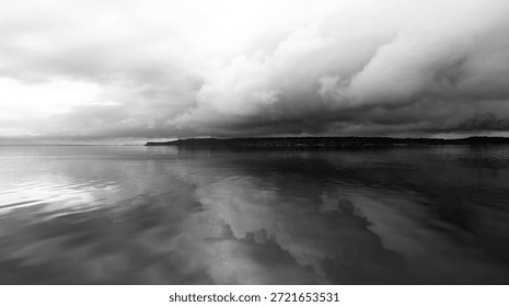 A black and white dramatic view of dark clouds reflected in the Rio Negro. A strip of the tropical forest in the background complements the drama. Rio Negro, Amazonia, Brazil.