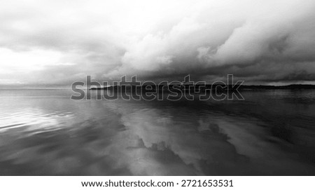 A black and white dramatic view of dark clouds reflected in the Rio Negro. A strip of the tropical forest in the background complements the drama. Rio Negro, Amazonia, Brazil.